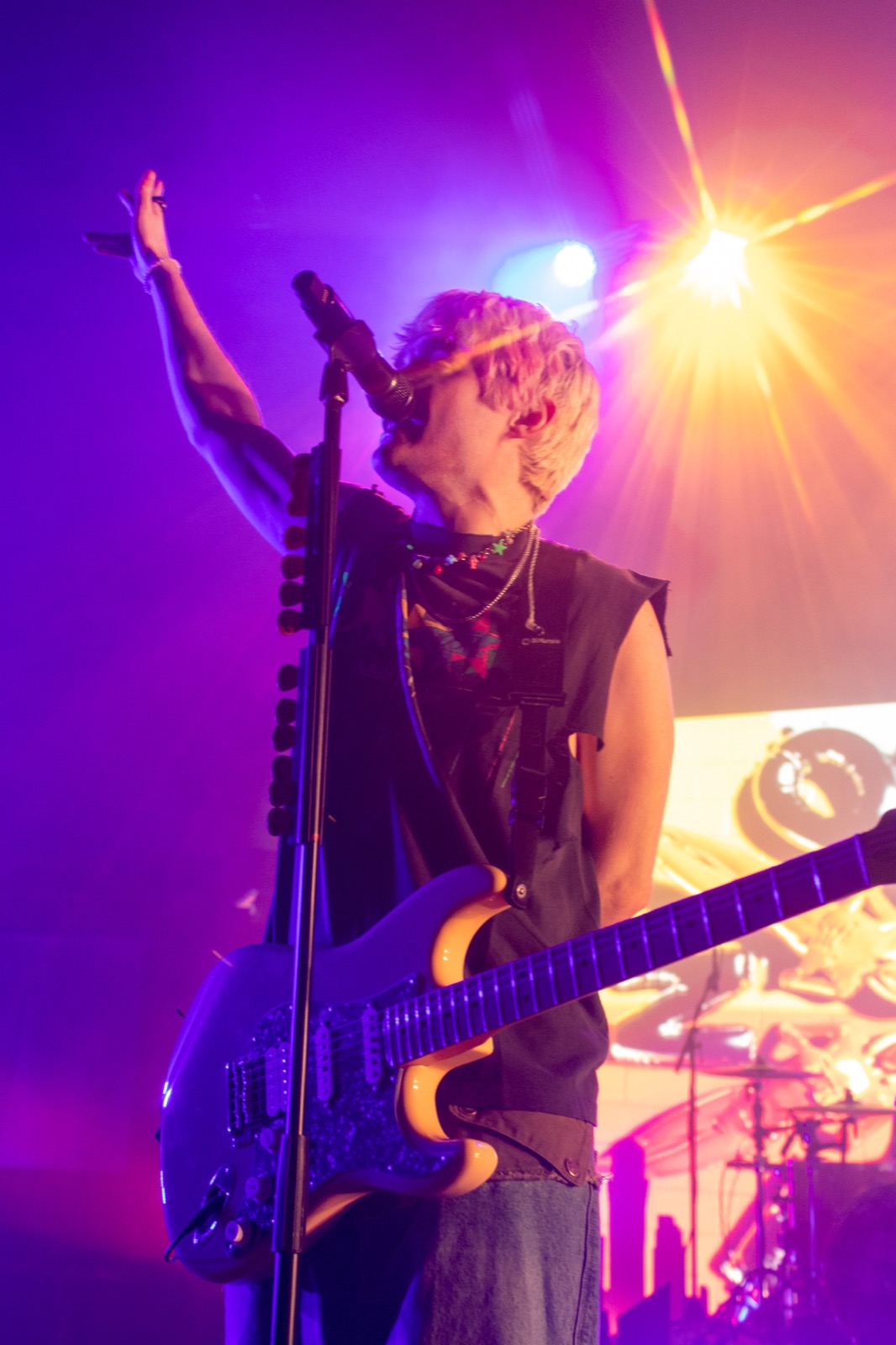 Guitarist singing into the mic under purple and orange stage lights